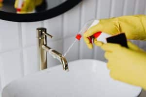 Person cleaning the sink in a bathroom: types of commercial cleaning businesses